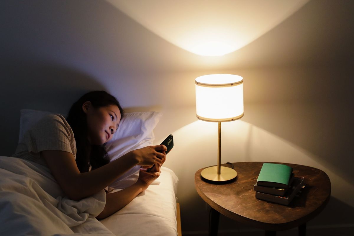 Ein Gast liegt abends im Hotelbett und schreibt auf dem Handy.